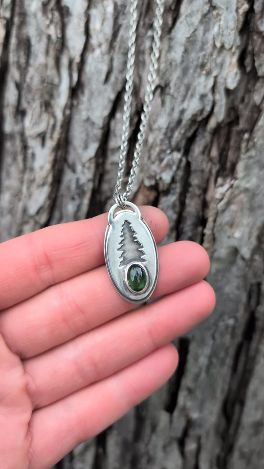 Green Tourmaline set with a beautiful pine tree cut out. I hand cut every single piece of these necklaces. This piece consists of two layers of silver. A solid oval sheet and then I drew the tree design onto the next oval and drilled a hole into the design then hand cut the tree out. Then solder them together along with the bezel and bail.